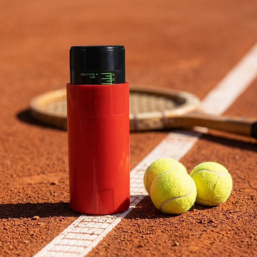 Presurizador rojo en una pista de tierra batida con pelotas de tenis